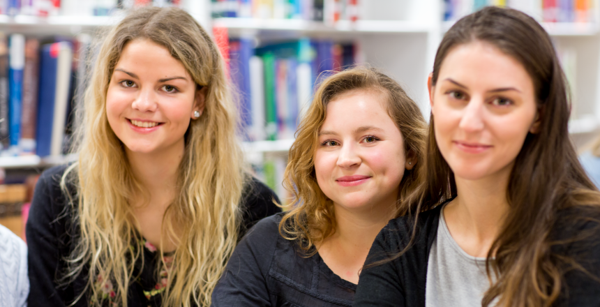 Tre glada studenter på bibliotek