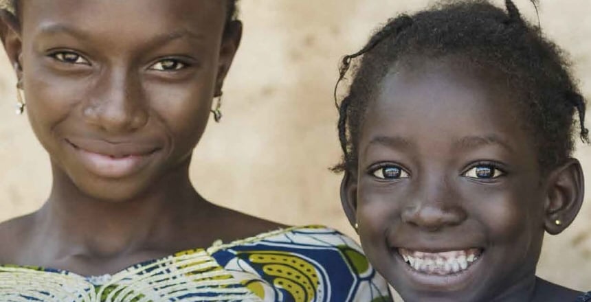 Två afrikanska flickor ler stort mot kameran.