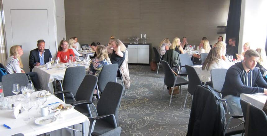 Flera människor som sitter kring dukade småbord och pratar och skrattar