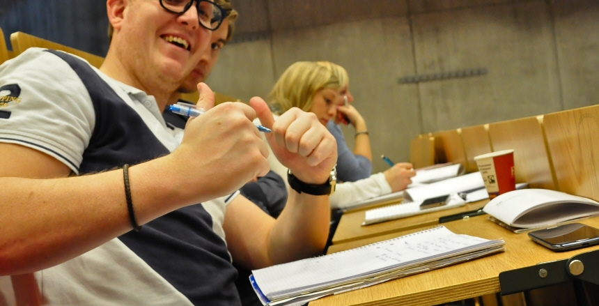 Manlig student som sitter vid skolbänk och gör tummarna upp mot kameran