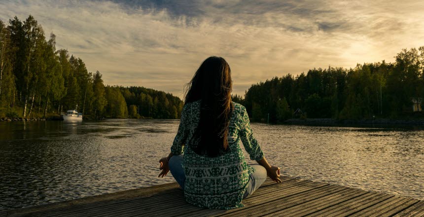 Kvinna sitter på en brygga med ryggen oemot vid vattnet