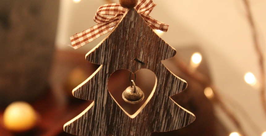 Julgransdekoration i trä som föreställer en gran. I granen har man sågat ut ett hjärta och där hänger en bjällra.