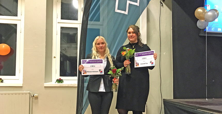 1 kvinna med långt ljust hår och 1 kvinna med mörkt uppsatt hår står framför Vårdförbundsflagga och håller i varsin blombukett och i stipendiet som är värt 2500 kr vardera