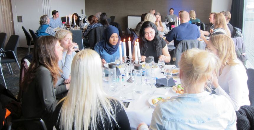 Studenter som sitter kring runda bord med vita dukar och tända ljus och äter examenslunch
