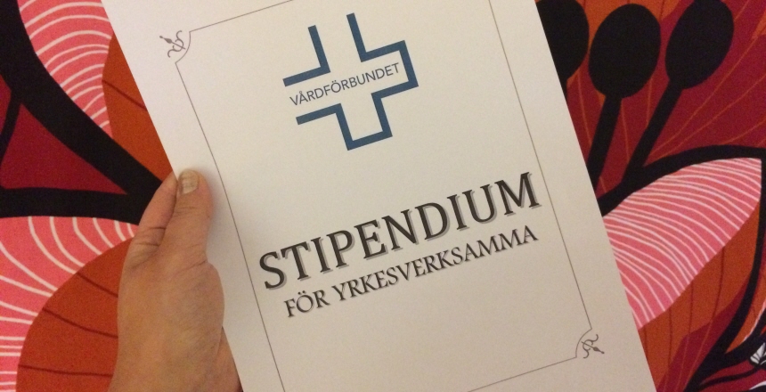 Hand som håller ett stipendium mot röd/blommig bakgrund