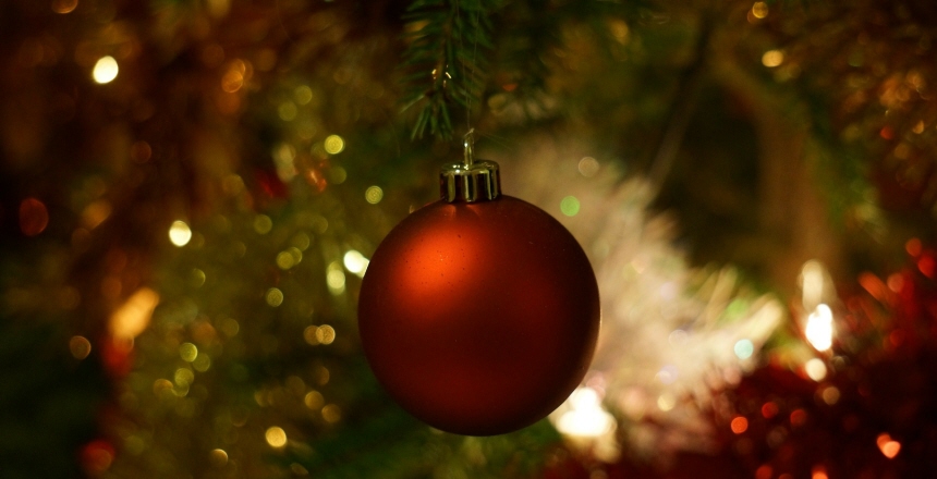 En röd julgranskula i förgrunden med glitter i rött, vitt och grönt i bakgrunden