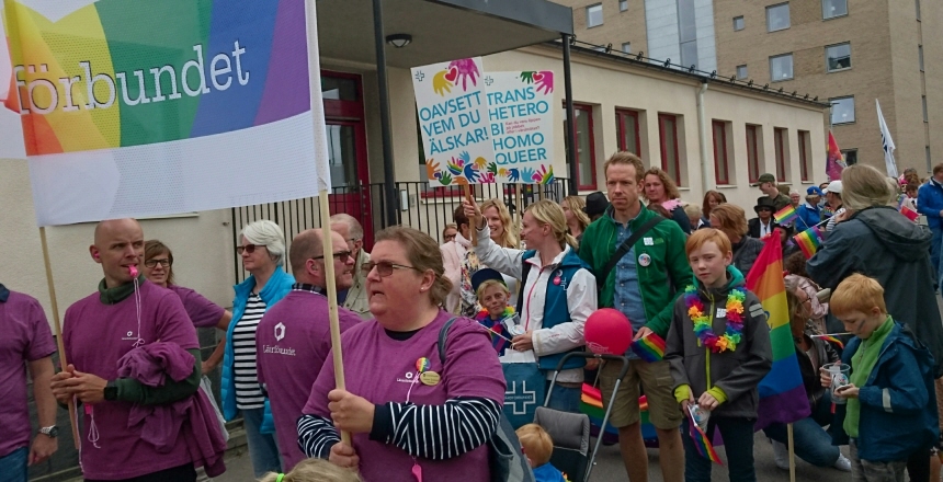 Pridefestival i Falkenberg. Människor med färgglada plakat som går tillsammans i ett långt tåg genom stan.