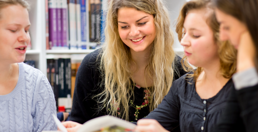 Grupp med fyra engagerade yngre kvinnor står runt en bok
