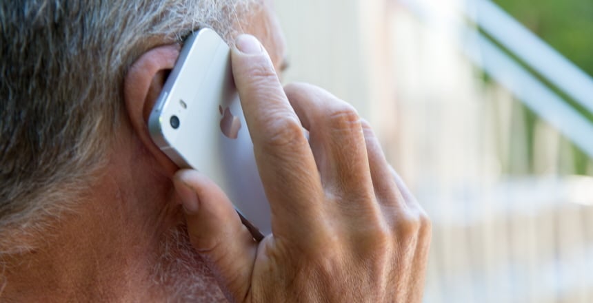Man håller mobiltelefon mot höger öra. Bilden är tagen bakifrån. Mannen har gråsprängt hår och lite skäggstubb.