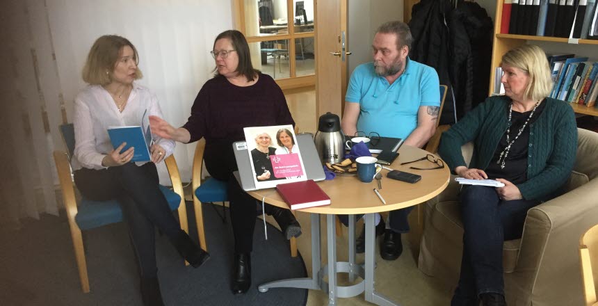 Fyra personer, tre kvinnor och en man sitter vid ett runt bord och diskuterar. På bordet finns det en dator, en termos och kaffekoppar.