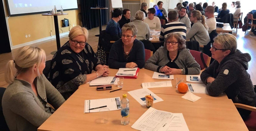 Fem kvinnor som sitter vid ett konferensbord och samtalar, i bakgrunden fler bord och människor